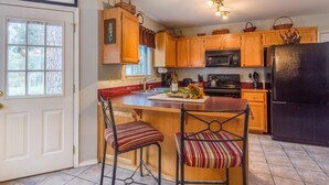 A kitchen with wooden cabinets, a black refrigerator, and a bar area with striped chairs. - Indio Road 16997 (Bend)