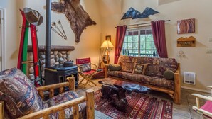 A cozy living room with a stone fireplace, a sofa, and a large fur wall. - Indio Road 16997 (Bend)
