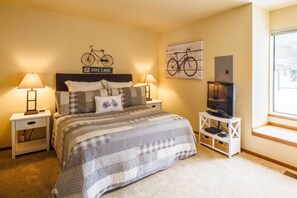 A bedroom with a bed, two bedside tables, a TV on a stand, and a window with a view. - Skyline Condo 13 (Bend)