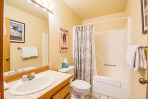 A bathroom with a sink, toilet, and bathtub. There is a shower curtain, a towel rack, and a framed poster on the wall. - Skyline Condo 13 (Bend)