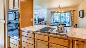 A kitchen with wooden cabinets, a built-in oven, a gas range, and a dining area with a table and chairs. - Skyline Condo 13 (Bend)
