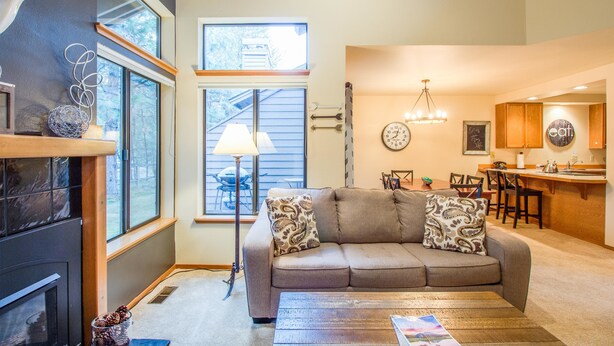 A living room with a sofa, a coffee table, and a fireplace. There is a dining area with a table and chairs, and a kitchen area with a counter and cabinets. - Skyline Condo 13 (Bend)