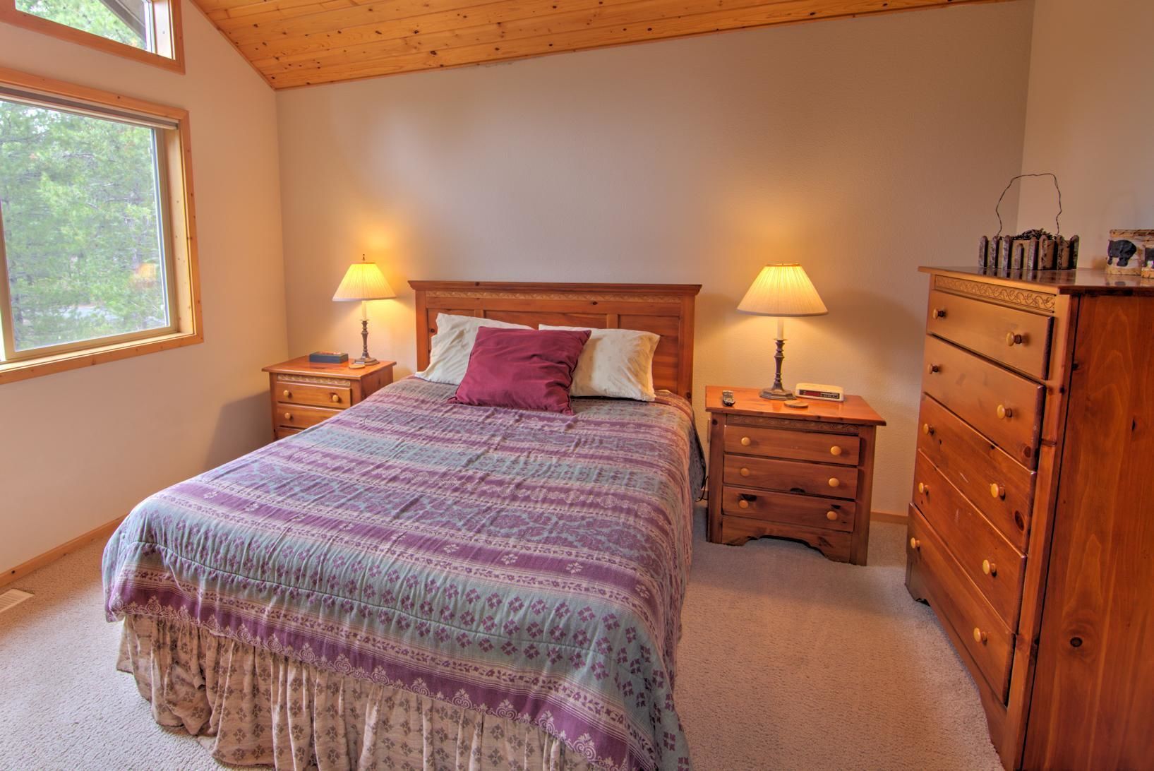 A bedroom with a large bed, two bedside tables with lamps, a dresser, and a window with a view of trees.