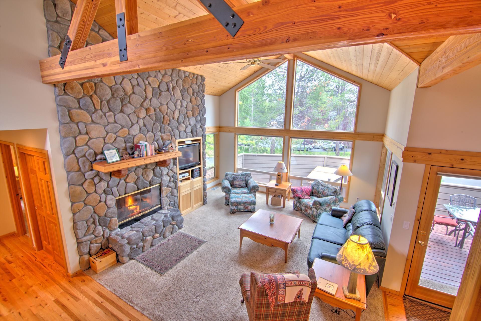 A cozy living room with a stone fireplace, large windows, and a comfortable seating area.