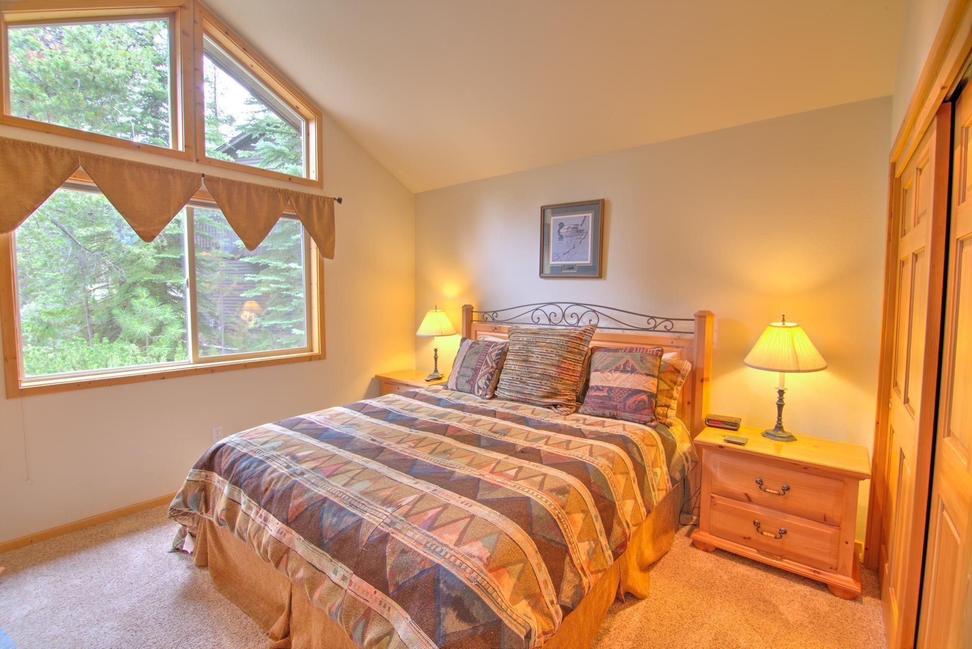 A bedroom with a bed, two bedside tables with lamps, a dresser, and a window with curtains.