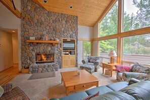 A cozy living room with a stone fireplace, a large window, and comfortable seating. - Rhododendron 9 (Bend)