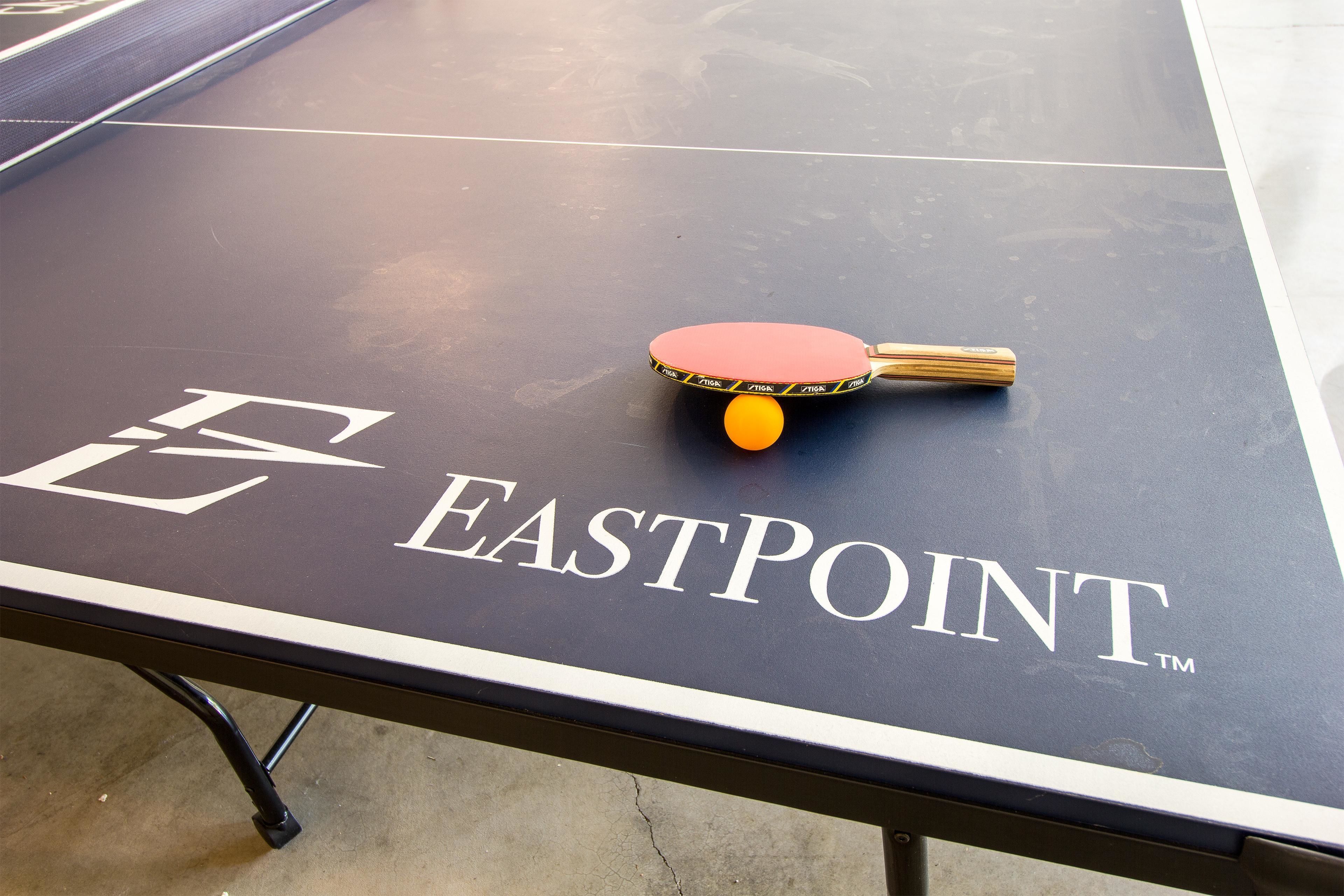 Une table de ping-pong avec une raquette et une balle, et le mot « EASTPOINT » inscrit sur la surface.