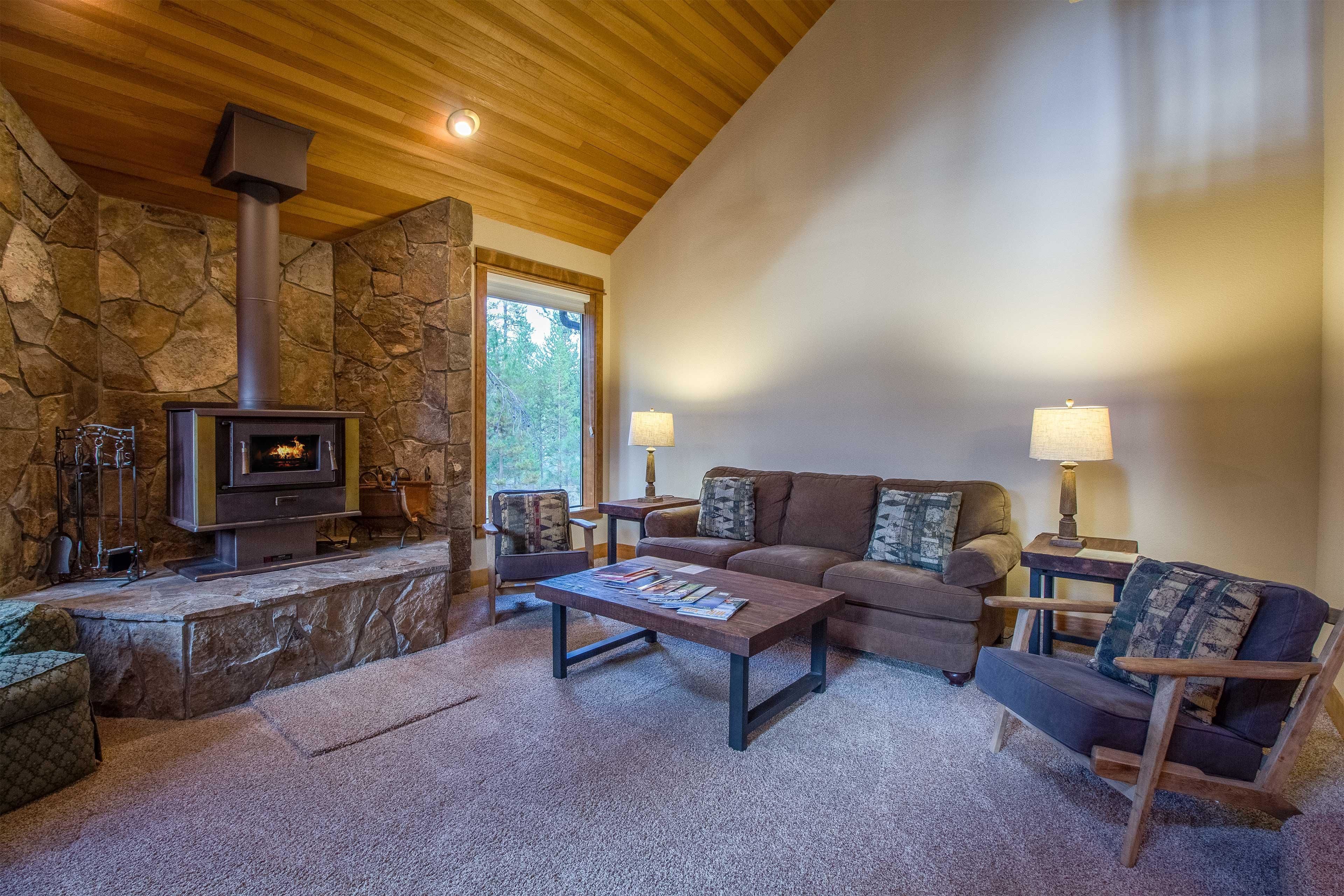 Una sala de estar acogedora con chimenea de piedra, techo de madera y un espacio de descanso cómodo con sofá y sillones.