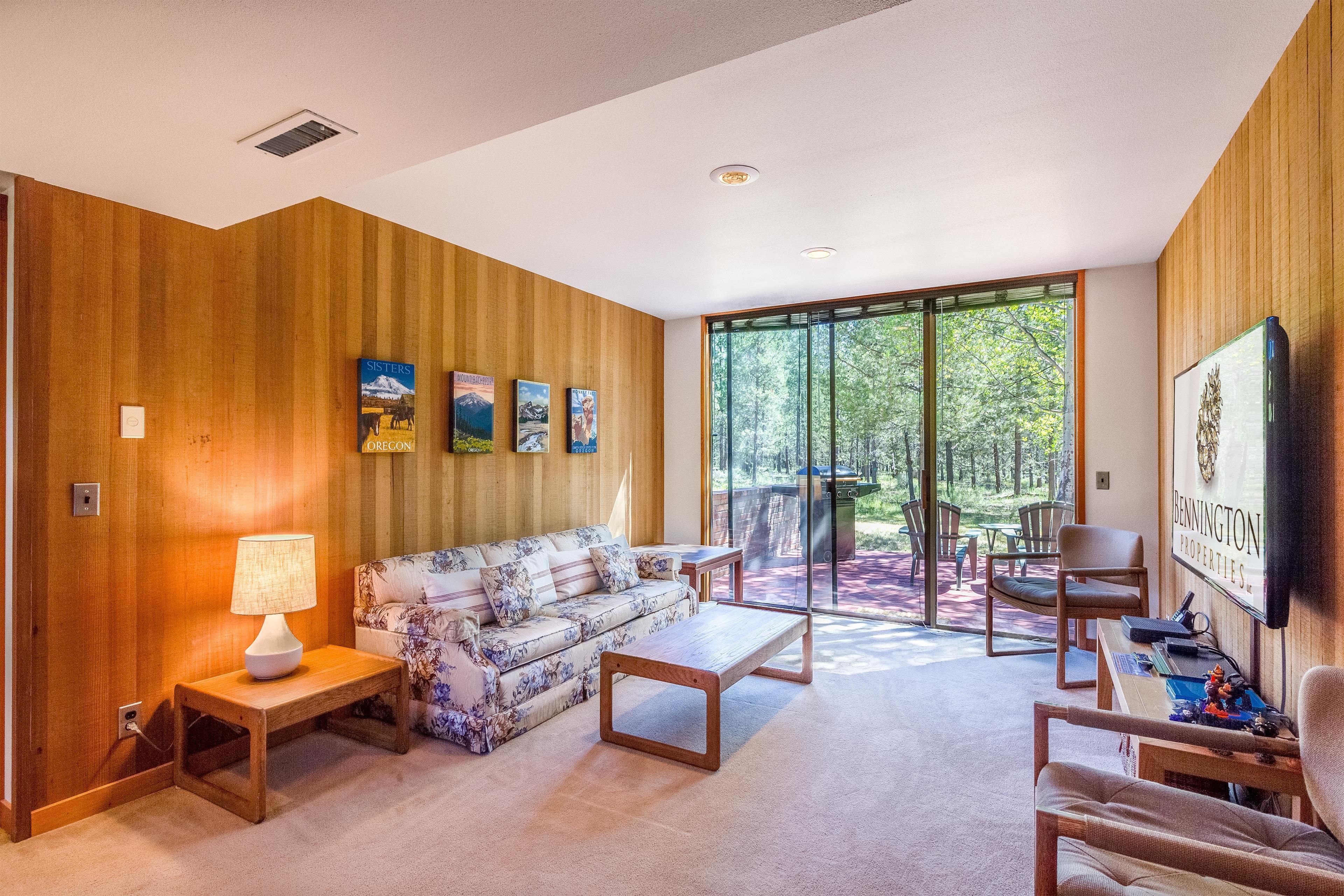 A modern living room with a wooden wall, a floral sofa, a coffee table, and a TV on the wall.