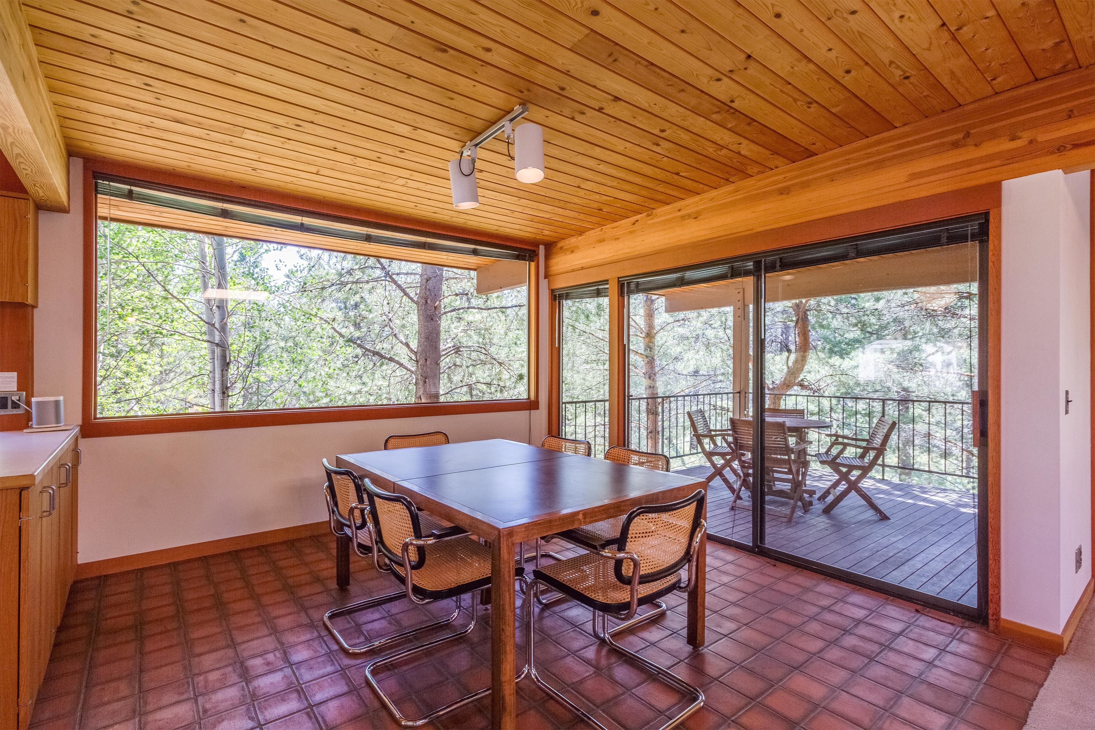 A wooden interior with a dining table and chairs, large windows, and a balcony with outdoor furniture.
