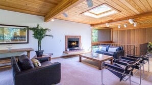A spacious living room with a fireplace, wooden ceiling, and a large window. - Wickiup 14 (Bend)