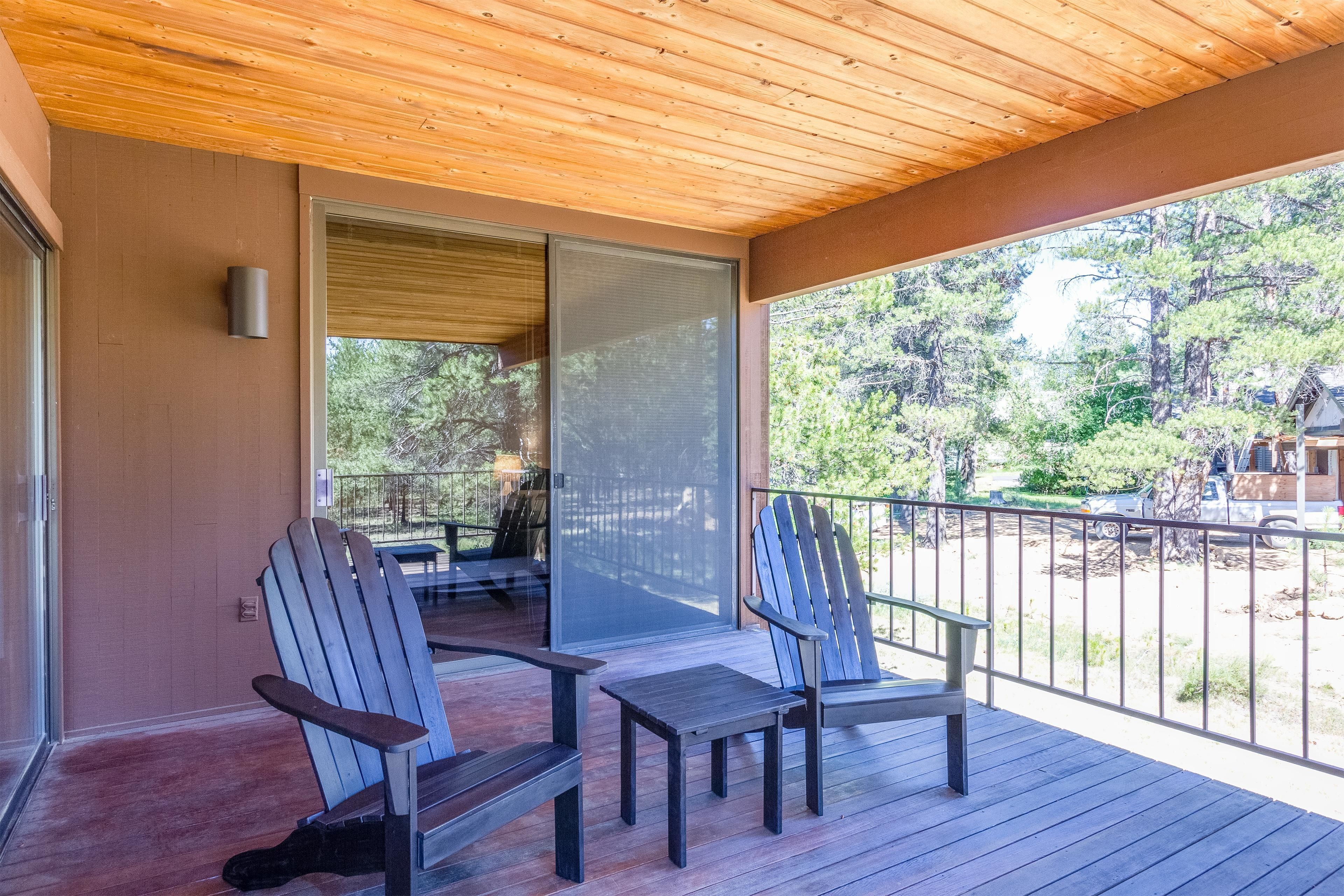 Eine Holzterrasse mit zwei Adirondack-Stühlen und einem Tisch mit Blick auf eine bewaldete Landschaft.