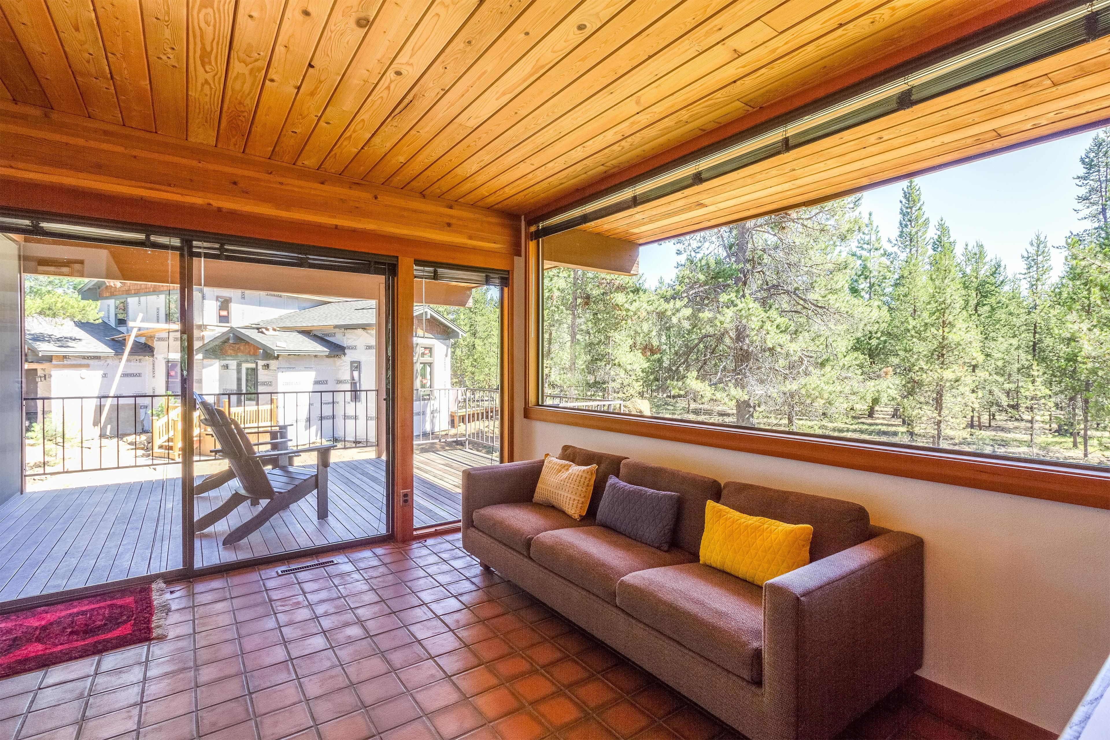 A wooden ceiling, a sliding glass door, a brown sofa with cushions, and a view of a forest.