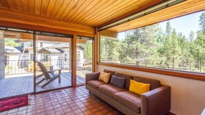 A wooden ceiling, a sliding glass door, a brown sofa with cushions, and a view of a forest. - Wickiup 14 (Bend)