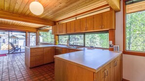 A modern kitchen with wooden cabinets, a large island, and large windows offering a view of the outdoors. - Wickiup 14 (Bend)