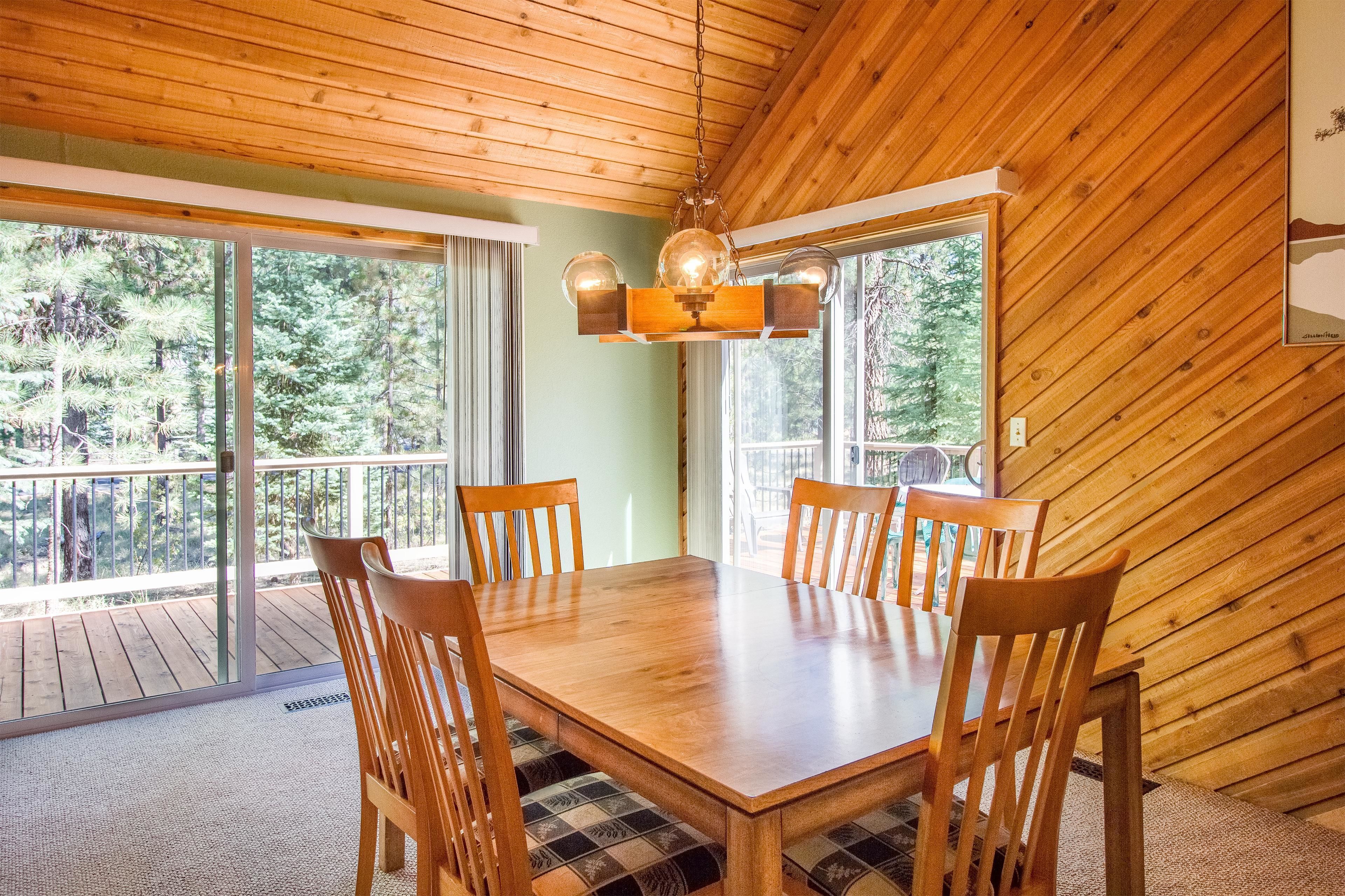 A dining area with a wooden table and chairs, large windows, and a wooden ceiling.