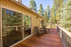 A wooden deck with chairs and a glass door leading to a screened-in area, surrounded by trees. - Pathfinder 1 (Bend)