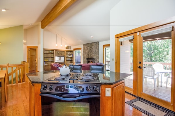 A modern kitchen with a central island stove, wooden cabinetry, and a dining area with a bench and chairs.