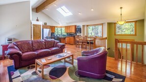 Un salón espacioso con techo alto, vigas de madera, un ventanal grande y una zona de estar acogedora con sofá y sillón de cuero.