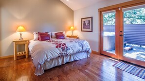 Un dormitorio con una cama grande, dos lámparas de noche, una mesita de noche de madera, un cuadro enmarcado en la pared y un ventanal corredero que da a un espacio exterior.