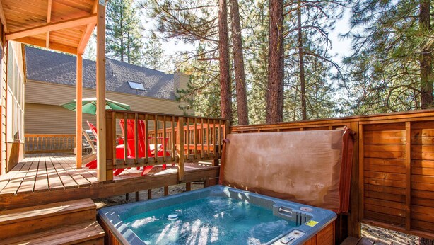 Un bain à remous sur une terrasse en bois, avec vue sur une maison et de grands arbres.