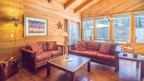 L’intérieur chaleureux d’un chalet avec des murs en bois, deux canapés, une table basse et de grandes fenêtres donnant sur le paysage extérieur.