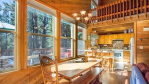 Une cabane en bois comprenant un coin repas, une cuisine et de grandes fenêtres donnant sur une forêt.