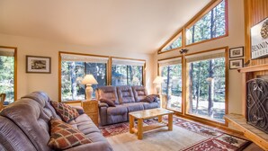 A cozy living room with leather sofas, a wooden coffee table, and large windows offering a view of trees. - Ashwood 4 (Bend)