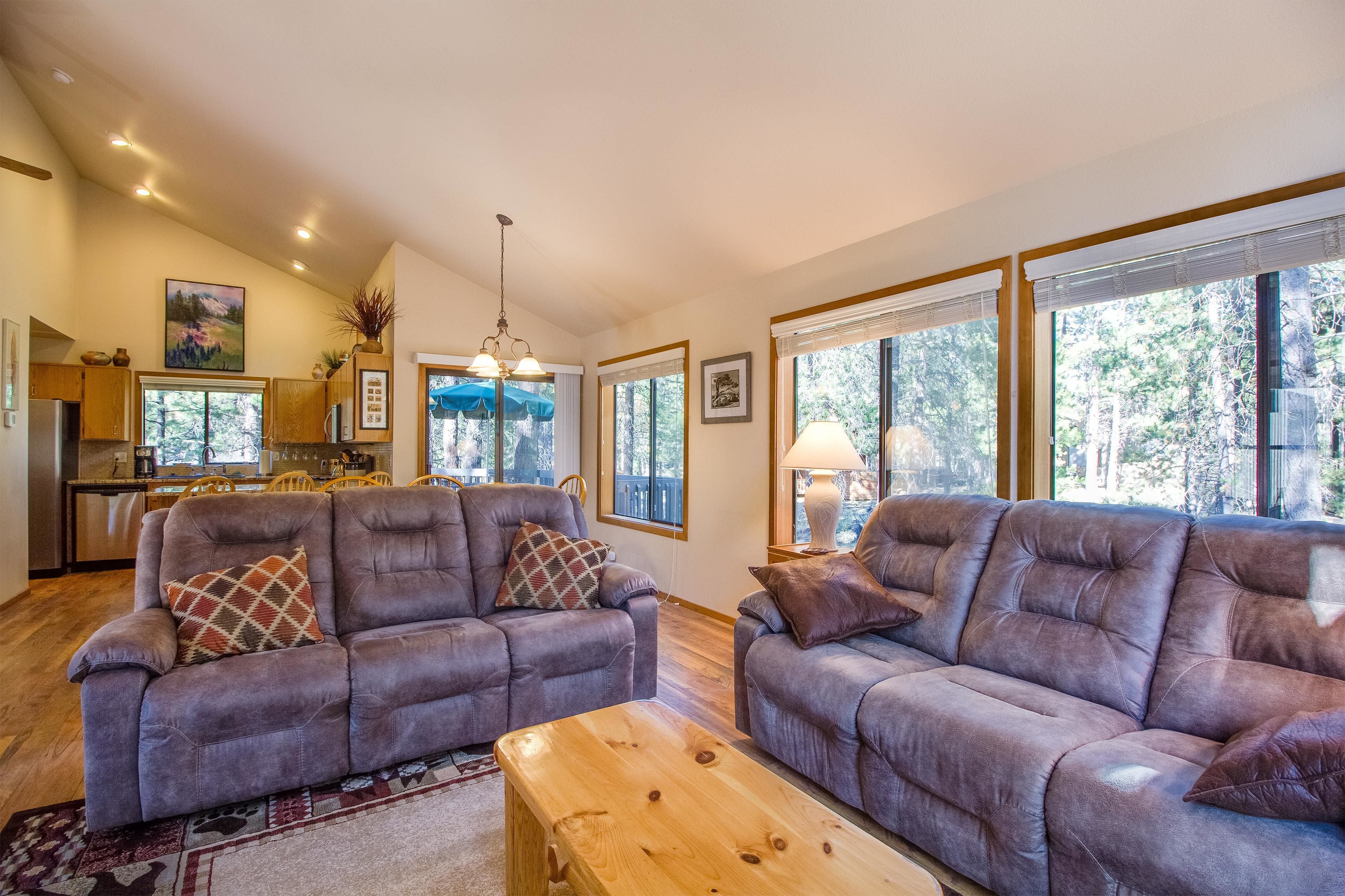 A spacious living room with two grey sofas, a wooden coffee table, and a kitchen in the background.