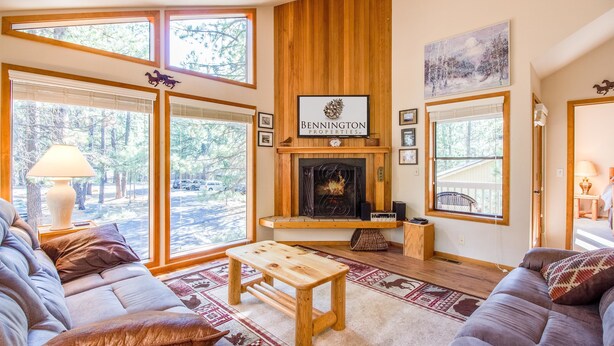 A cozy living room with a fireplace, large windows, and a wooden accent wall. - Ashwood 4 (Bend)