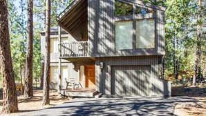 A modern cabin with a balcony, large windows, and a garage, surrounded by tall pine trees. - Ashwood 4 (Bend)