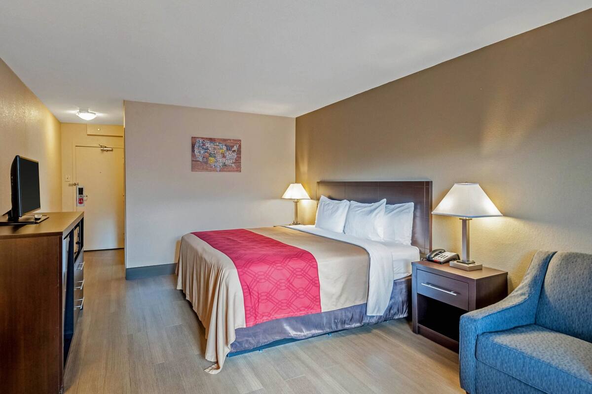 A hotel room with a bed, bedside lamps, a desk with a TV, and a chair.