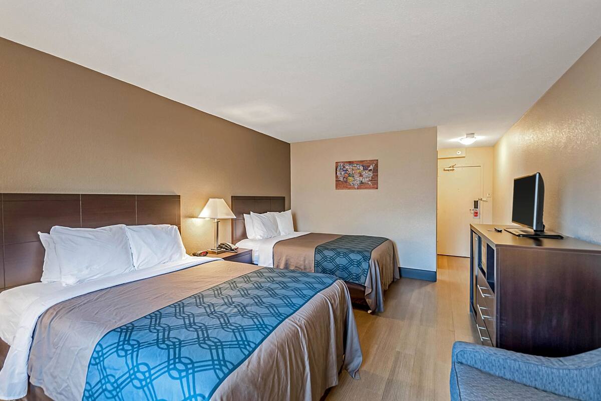 A hotel room with two beds, a desk, a TV, and a chair.