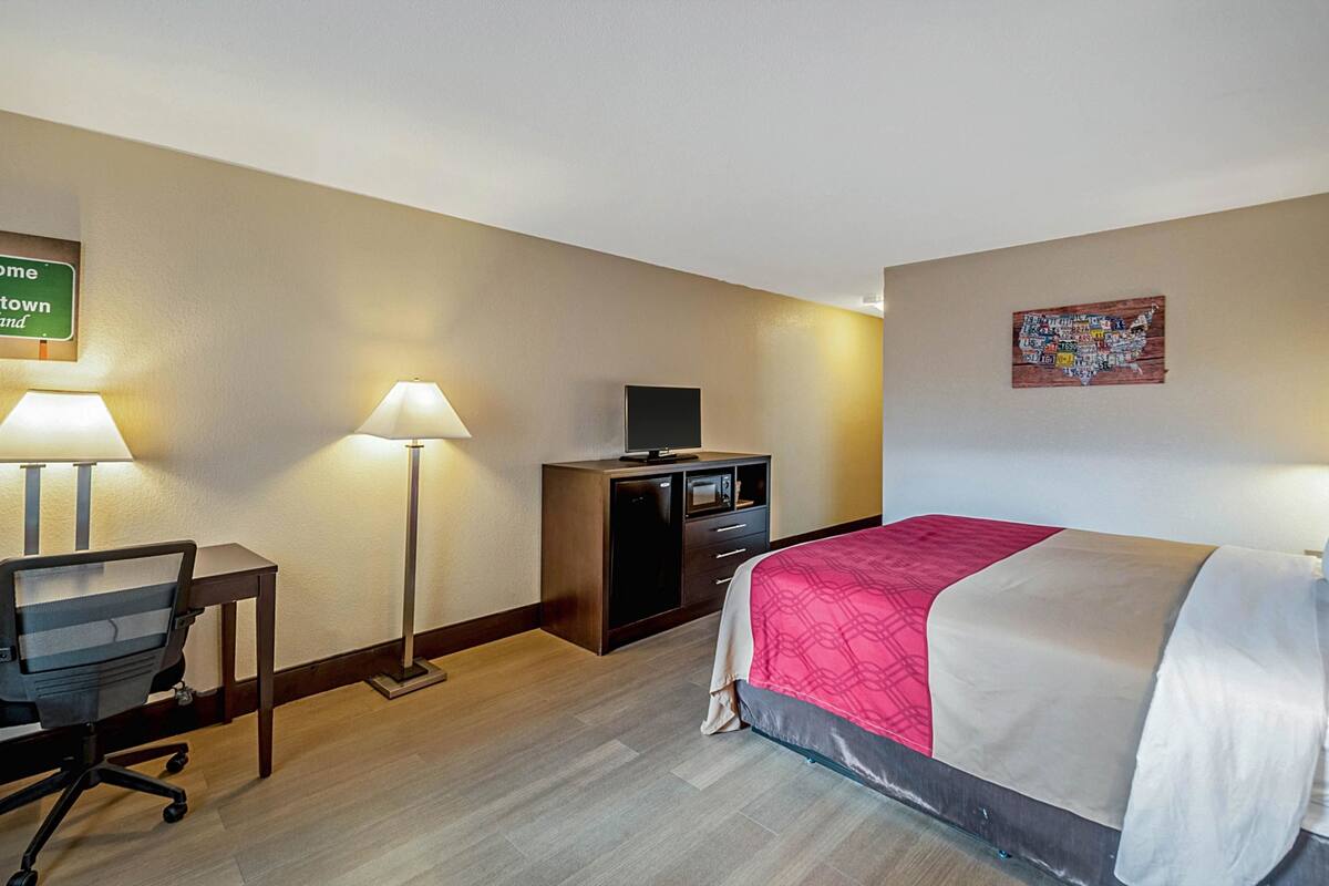 A hotel room with a bed, desk, chair, lamp, TV, and a map on the wall.