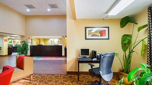 Een hotellobby met een receptiebalie, een bureaustoel en een rode bank, plus potplanten.