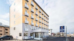 Ein mehrstöckiges Hotel mit Klimaanlagen auf jedem Balkon, einem Parkplatz und einem Schild für Comfort Inn Yokohama.