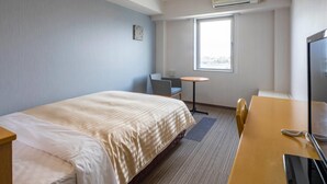 Ein Hotelzimmer mit einem Bett, einem Schreibtisch mit Computer, einem Sessel, einem kleinen Tisch und einem Fenster.
