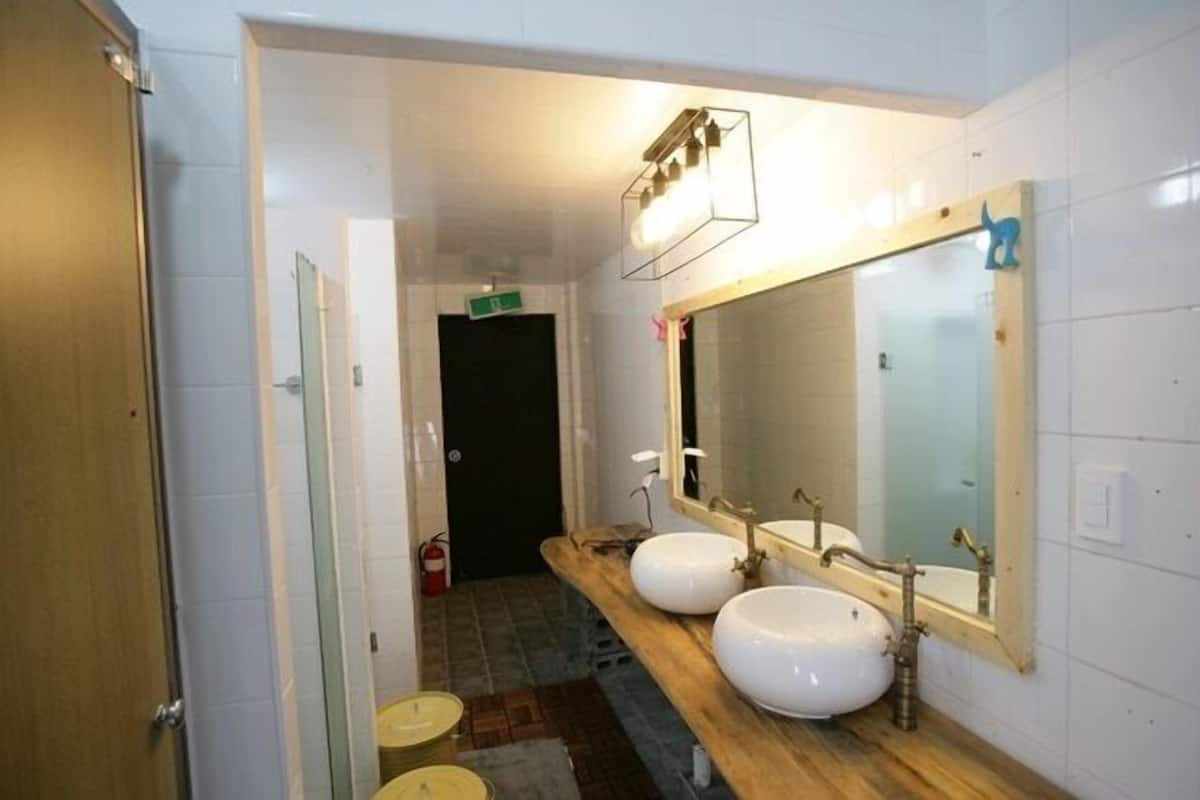 Une salle de bain avec deux lavabos, un meuble-lavabo en bois, un grand miroir et un luminaire placé au-dessus du miroir.