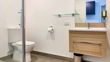 A modern bathroom with a toilet, glass shower enclosure, and a wooden vanity with a sink.