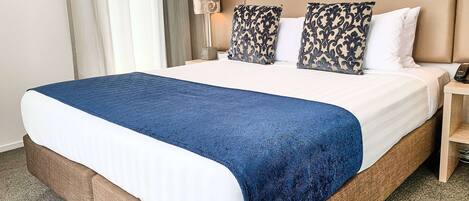 A hotel room with a large bed, a bedside table, a lamp, and a curtain.