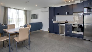 Una cocina moderna con armarios oscuros, electrodomésticos de acero inoxidable y un comedor con sofá azul y sillas color beige.