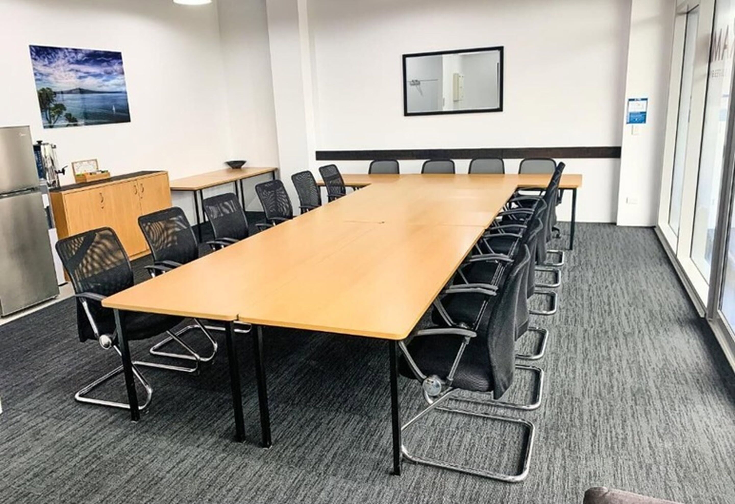 Un salón de conferencias con una larga mesa, sillas negras, un armario de madera y un cuadro en la pared.