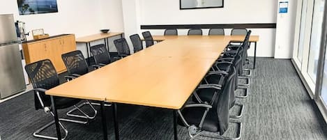 Un salón de conferencias con una larga mesa, sillas negras, un armario de madera y un cuadro en la pared.