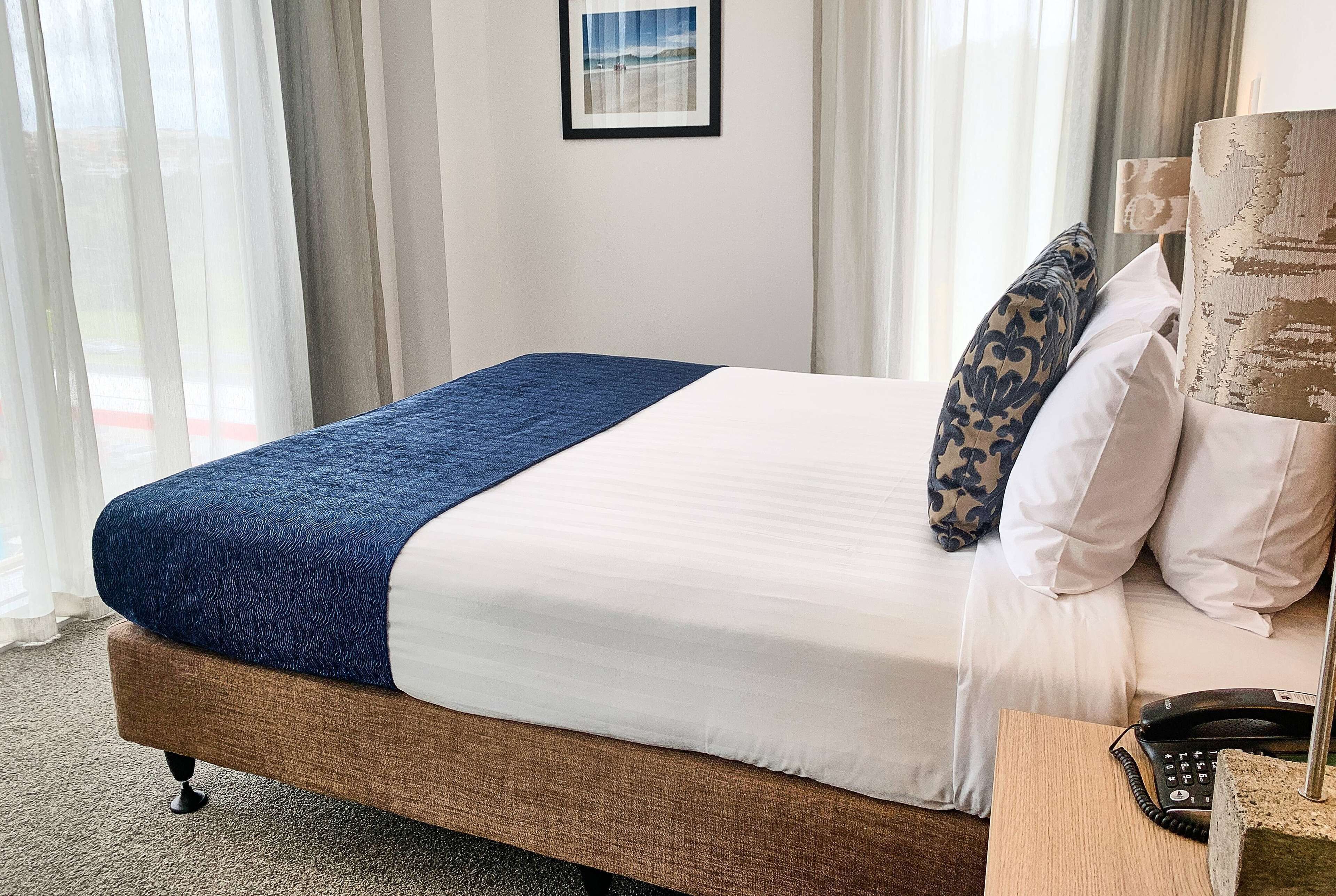Una cama bien tendida con una manta azul, almohadas blancas y un cabecero de madera.