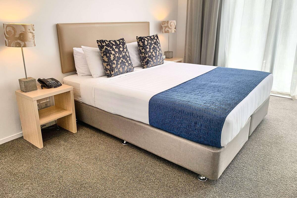 Ein Hotelzimmer mit einem großen Bett, zwei Nachttischlampen, einem Nachtischtelefon und einem kleinen Holznachttisch.
