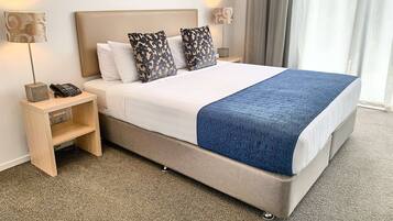 A neatly made bed with a blue blanket, two patterned pillows, a bedside lamp, and a phone on a wooden nightstand.