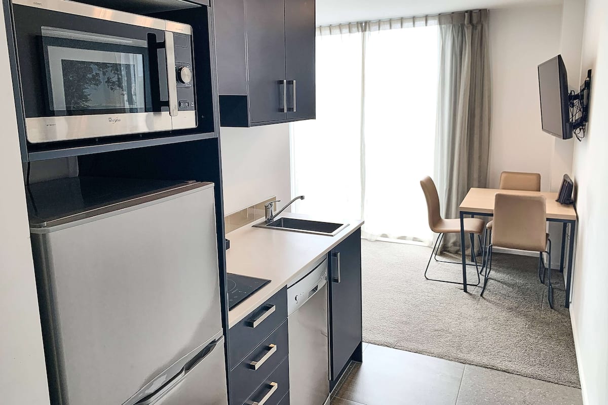 Compact kitchenette with microwave, refrigerator, and sink, adjacent to a dining area with a table and two chairs.
