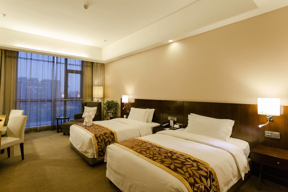 Habitación de hotel con dos camas, un escritorio, una silla y un ventanal con cortinas.