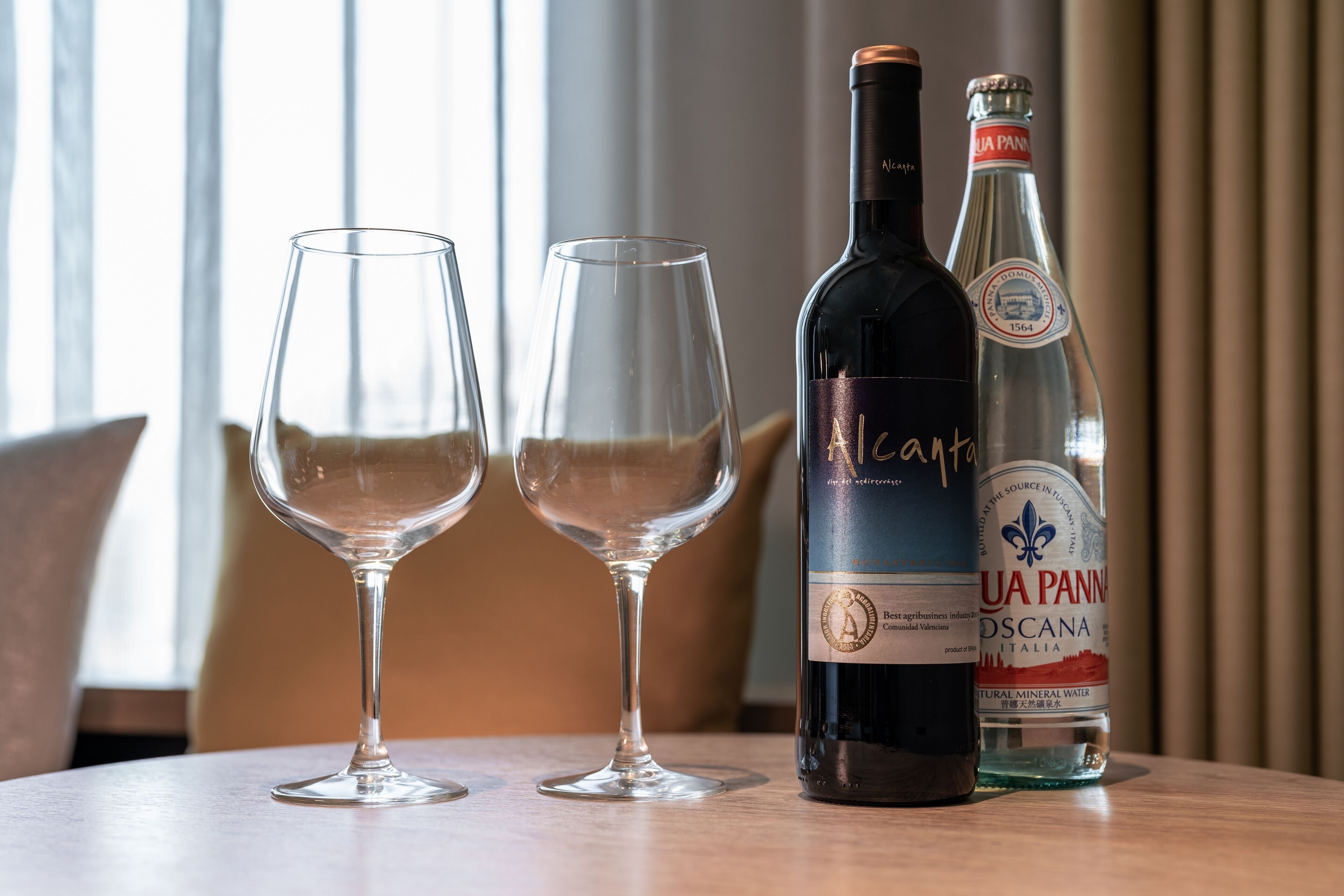 Two wine glasses and two bottles on a table.