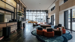 A modern lobby with a reception desk, seating area, and large windows offering a view of the street. - Greet Inn (Kaohsiung)